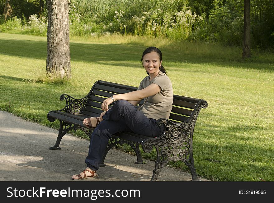 A smiling woman sitting on a bench in a public park