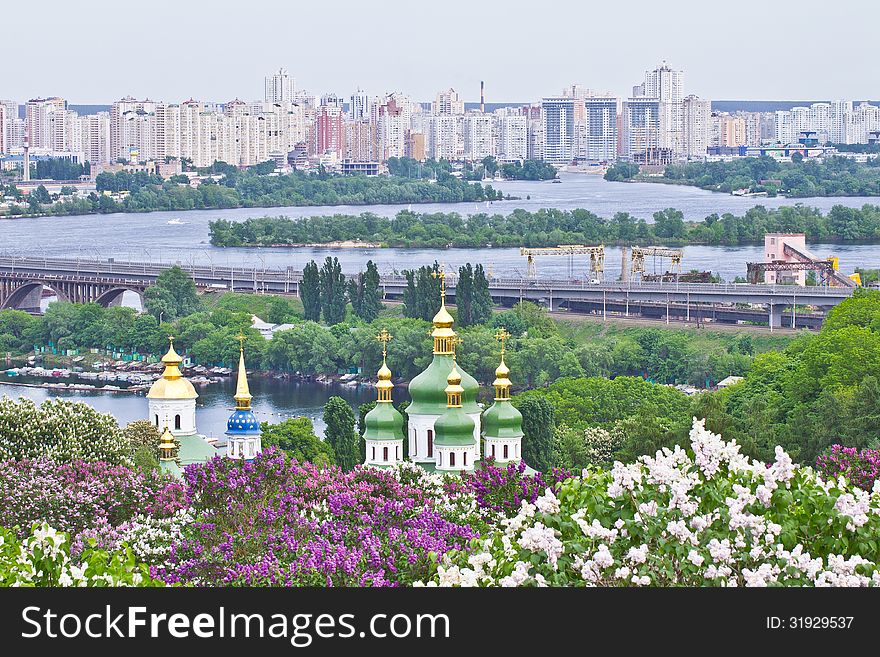 View on domes of Vydubychi monastery, blooming trees and high buildings on the left bank of Dniper in Kiev, Ukraine. View on domes of Vydubychi monastery, blooming trees and high buildings on the left bank of Dniper in Kiev, Ukraine