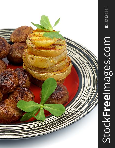 Roasted Meatballs and Stack of Grilled Potato with Greens on Red Striped Plate closeup on white background. Roasted Meatballs and Stack of Grilled Potato with Greens on Red Striped Plate closeup on white background