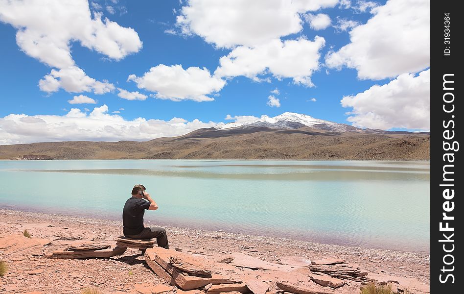 Man sitting on the shore of lagoon Celeste and talking on phone, Bolivia. Man sitting on the shore of lagoon Celeste and talking on phone, Bolivia