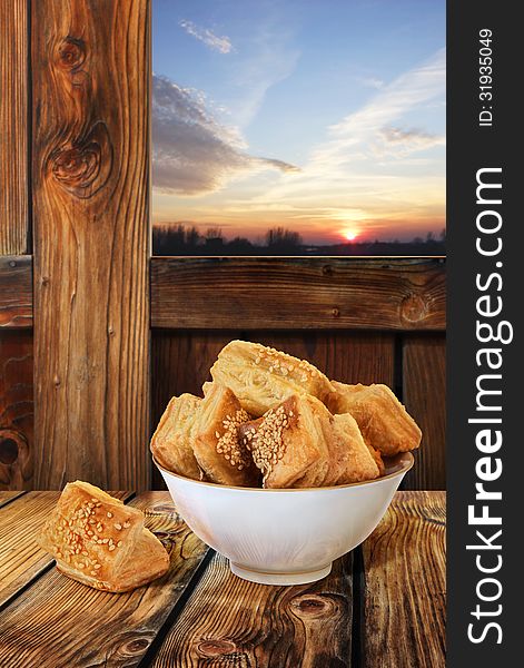 Small Square Sesame Puff Pastry Zu-Zu, served in white Porcelain Bowl, isolated with precise Clipping path, set in a wooden rustic farm ambient, with sunset sky in the background window. Small Square Sesame Puff Pastry Zu-Zu, served in white Porcelain Bowl, isolated with precise Clipping path, set in a wooden rustic farm ambient, with sunset sky in the background window.