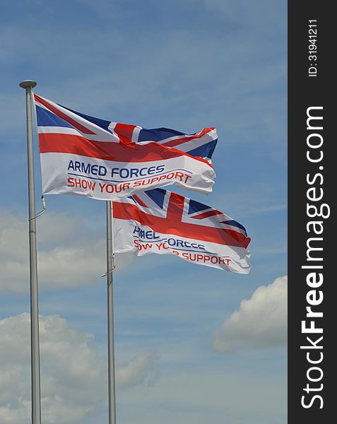 Two Union Jack flags with the words armed forces show your support flying in the wind, on a cloudy summers day background. Two Union Jack flags with the words armed forces show your support flying in the wind, on a cloudy summers day background