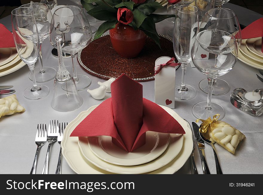 Red and white theme wedding breakfast dining table setting with red table napkins in bishop style folds, for weddings or Valentine day banquet meal.