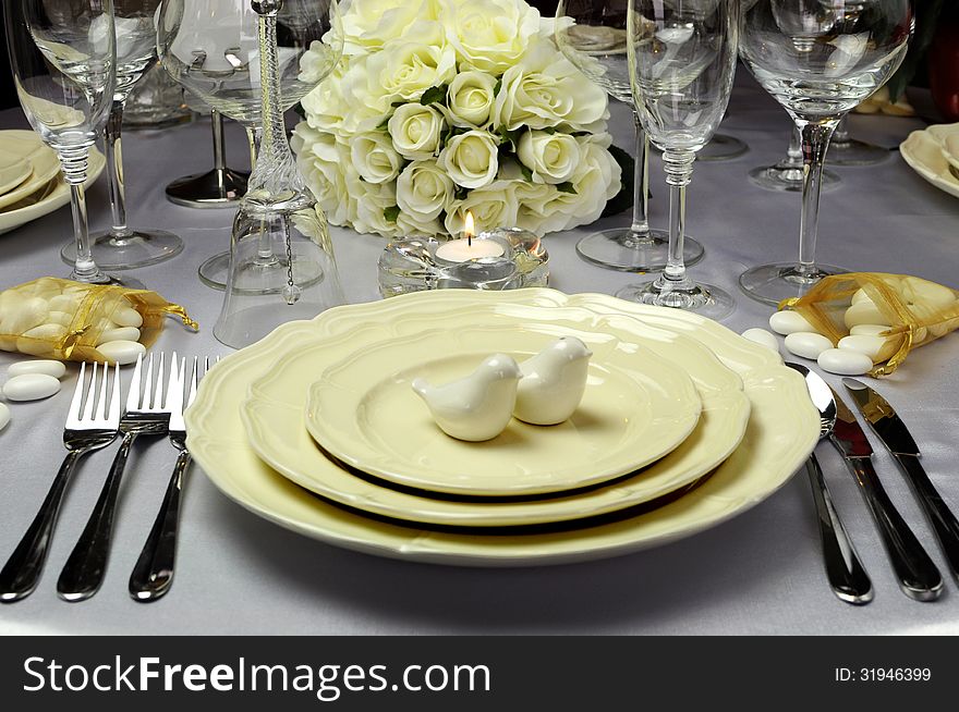 Close up of detail on wedding breakfast dining table setting with dove shape salt and pepper shakers on beautiful china plates with white roses bouquet in background. Close up of detail on wedding breakfast dining table setting with dove shape salt and pepper shakers on beautiful china plates with white roses bouquet in background