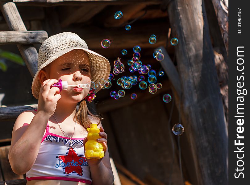 Little girl in a hat blowing soap bubbles