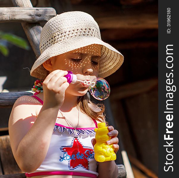 Little girl in a hat blowing soap bubble