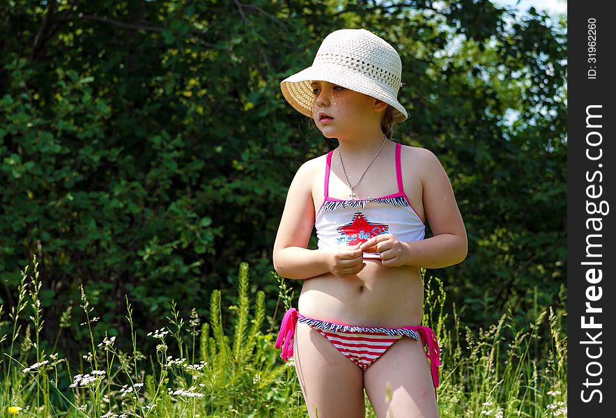 Little girl in a hat standing on a meadow