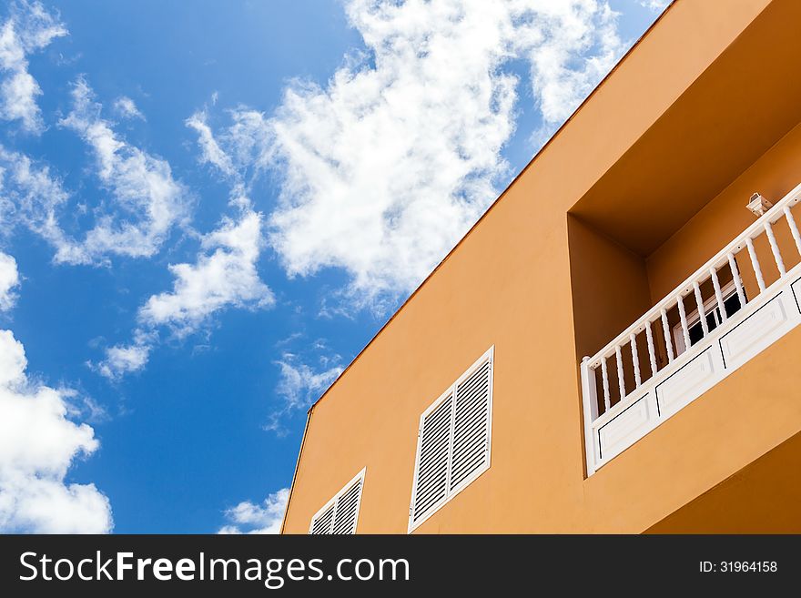 House in city, blue sky and apartment building over white clouds. Sunny day, orange wall and balcony, architecture on Tenerife, Canary Islands. House in city, blue sky and apartment building over white clouds. Sunny day, orange wall and balcony, architecture on Tenerife, Canary Islands