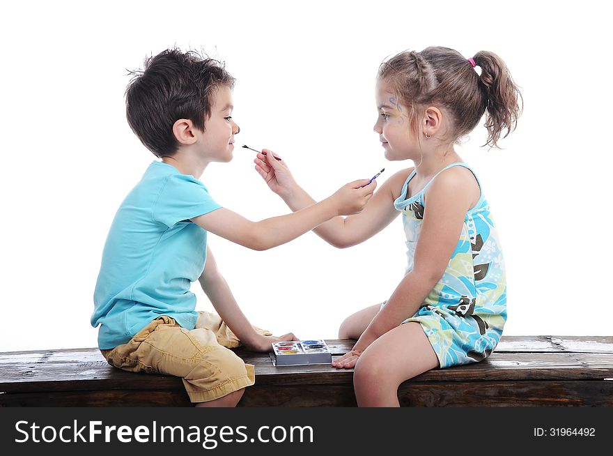 Boy and girl face painting one another siting on a bench in a studio on white background
