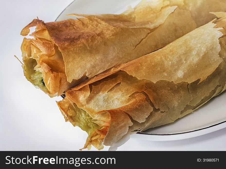 Roll pie with Spinach and cheese, on white oval plate with tiny blue rim. Roll pie with Spinach and cheese, on white oval plate with tiny blue rim.