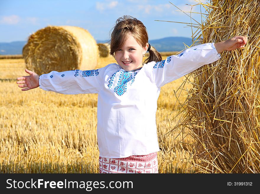 Small rural girl on harvest field with straw bales