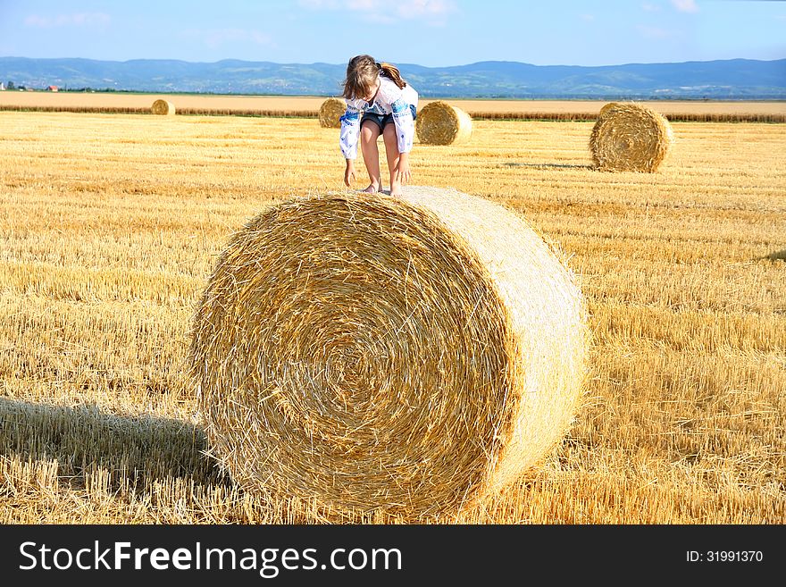 Girl on the straw after harvest field with straw bal