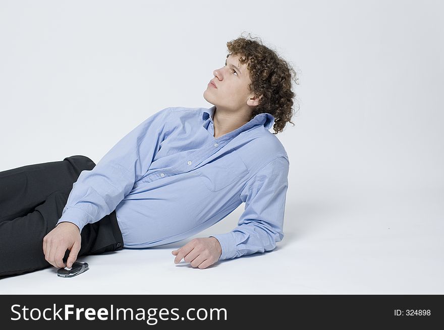 (Boy in relaxed office attire) Boy lying down, leaning up on one arm with a cellphone beside him. (Boy in relaxed office attire) Boy lying down, leaning up on one arm with a cellphone beside him