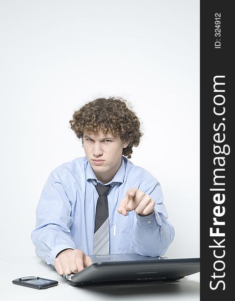 (Boy in relaxed office attire) Boy pointing straight into camera is sitting at a desk with a laptop and palm. (Boy in relaxed office attire) Boy pointing straight into camera is sitting at a desk with a laptop and palm