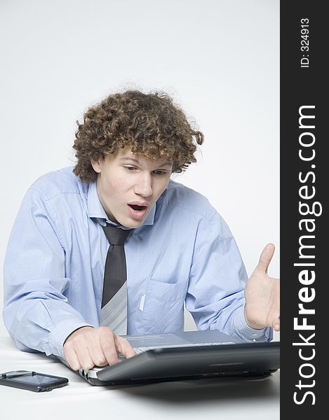 (Boy in relaxed office attire) Boy sitting at a table with a laptop and palm is looking at the laptop with a surprised expression. (Boy in relaxed office attire) Boy sitting at a table with a laptop and palm is looking at the laptop with a surprised expression