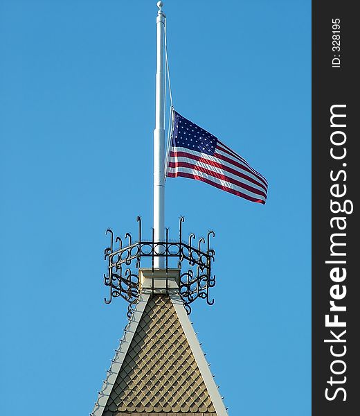 USA Flag at half mast on top of building structure against bright blue sky