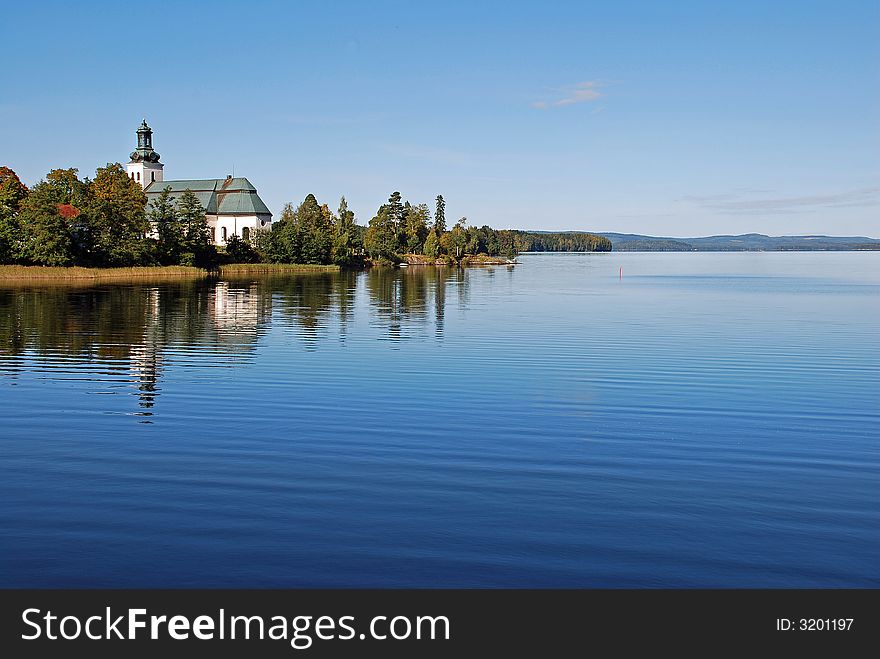 A lake in sweden,reflection of the church and trees in the calm water.Scenic view of a little hills in the background. A lake in sweden,reflection of the church and trees in the calm water.Scenic view of a little hills in the background.