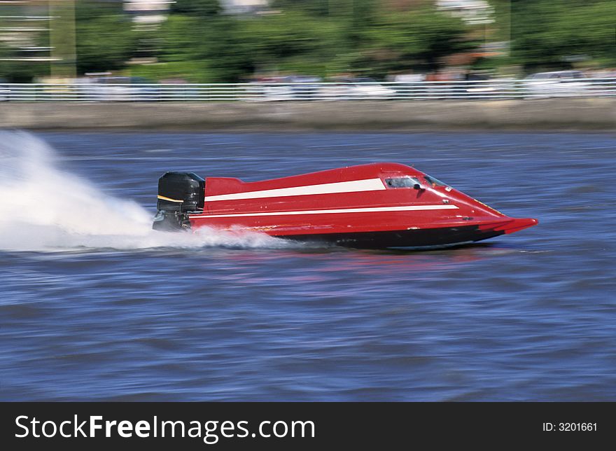 A red outboard of competition at full speed on blue water of a river.