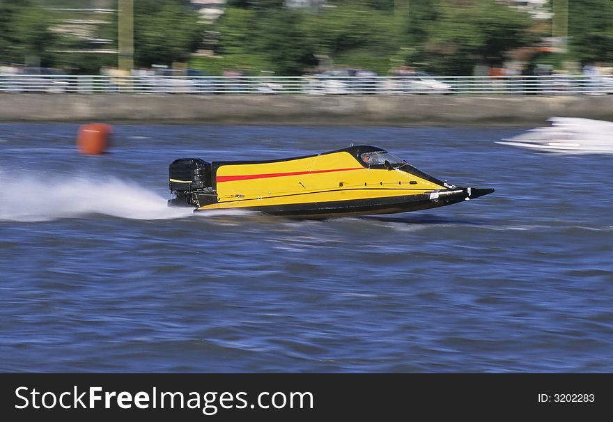 A yellow outboard of competition at full speed on blue water of a river.