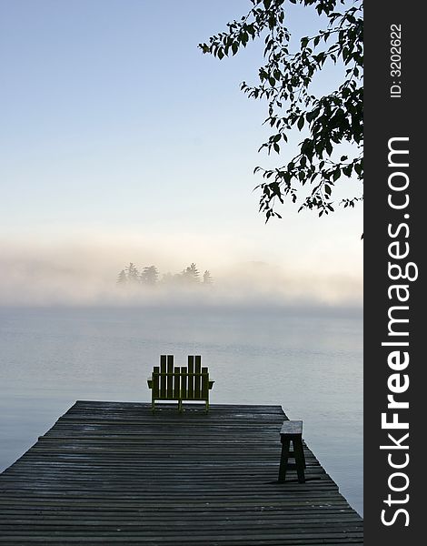 A chair by a misty lake early in the morning. A chair by a misty lake early in the morning.