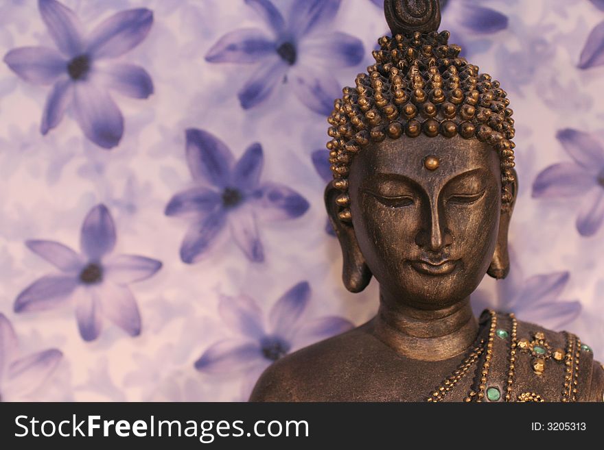 Meditating buddha statue with lilac flower background