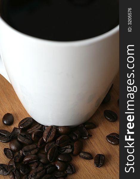 Black coffee in a white mug with roasted coffee beans spread around,seen from above
