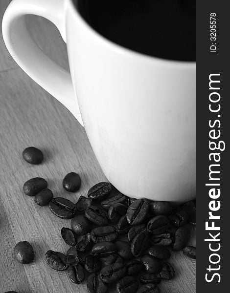 Black coffee in a white mug with roasted coffee beans spread around,black and white image