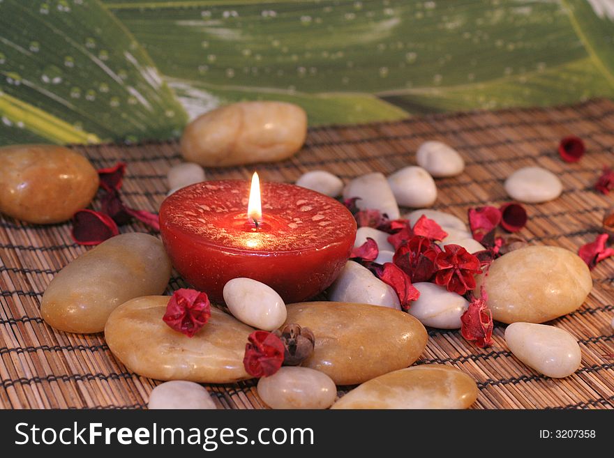 Red candle sourrounded with stones and flowers