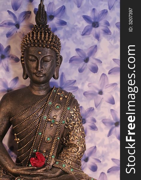 Meditating buddha statue with lilac background holding a red flower. Meditating buddha statue with lilac background holding a red flower