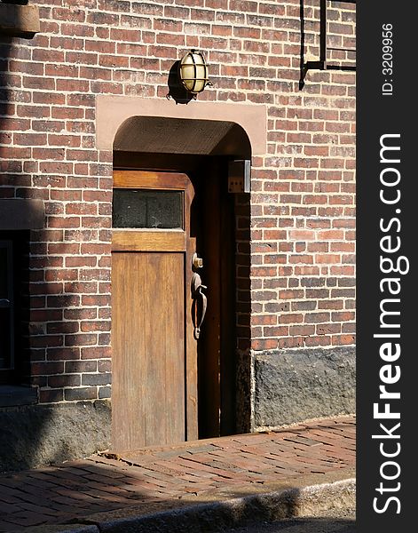 Old wooden basement door inset in brick wall, strong shadow in beacon hill area of boston