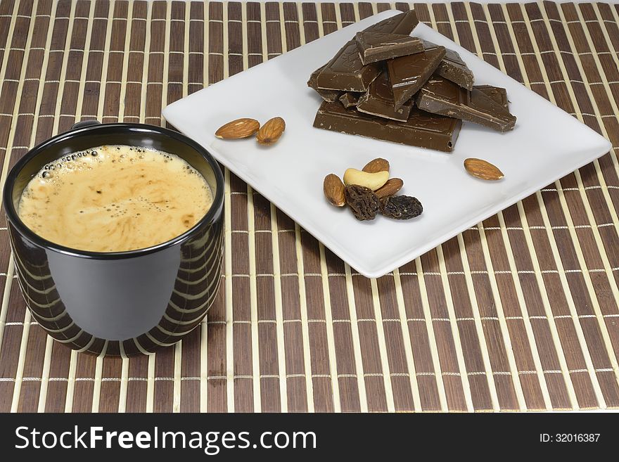 Dark nut chocolate and raisin on a white plate to a cup of morning coffee. Dark nut chocolate and raisin on a white plate to a cup of morning coffee