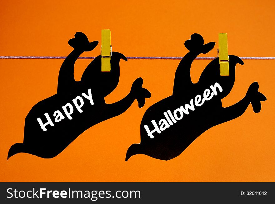 Happy Halloween greeting written across black ghosts cards hanging from pegs on a line against an orange background.