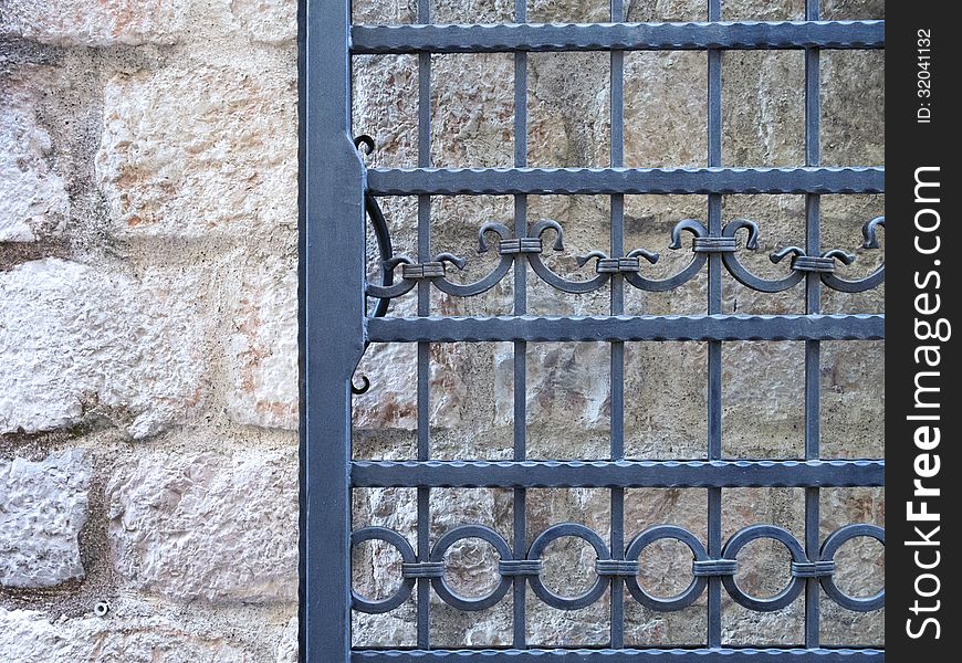 Fragment of wrought-iron door frame over ancient stone wall