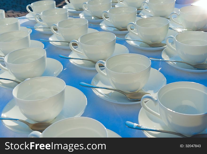 Stacked Empty Teacups With Teaspoons At A Function Over White Ba