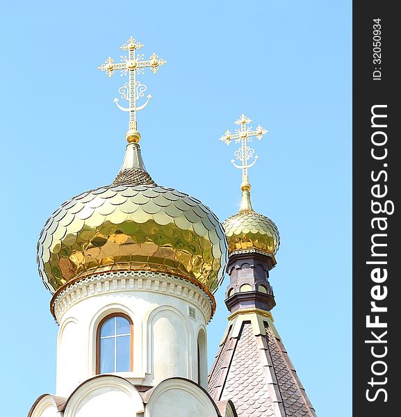 Golden dome of the Orthodox church on the blue sky background partially covered with snow.