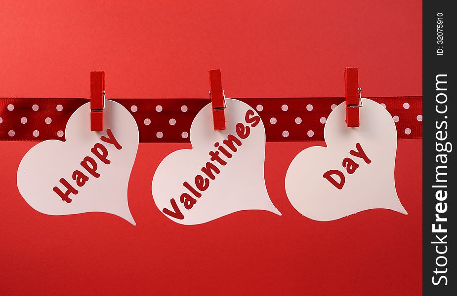 Happy Valentines Day message greeting written across white heart tags hanging from red pegs on a line