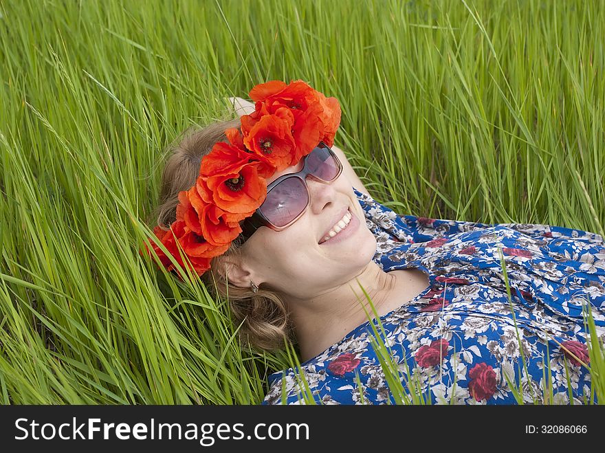 Young woman in wreath red poppies lying in green grass. Young woman in wreath red poppies lying in green grass