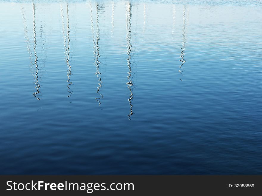 Masts of yachts reflected in blue water. Masts of yachts reflected in blue water