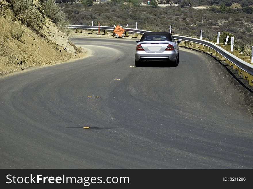 Silver Covertible driving on newly paved winding road. Silver Covertible driving on newly paved winding road