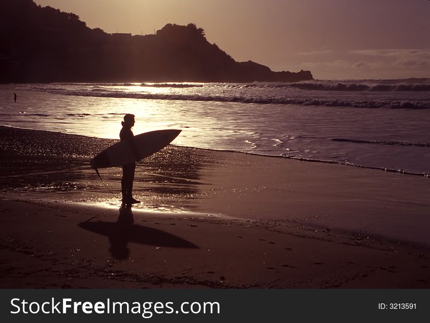 A silhouette of an early morning surfer on a beautiful shoreline. A silhouette of an early morning surfer on a beautiful shoreline.