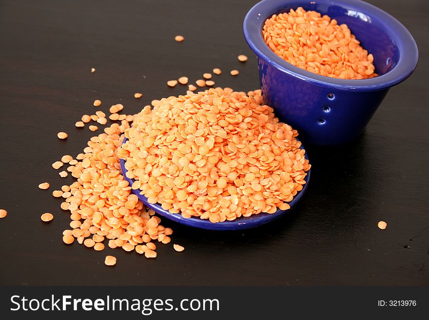 Lentils overflowing from blue ceramic bowl on a brown surface