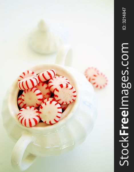 Red and white hard candies in white sugar bowl, lid and more candies in background. Red and white hard candies in white sugar bowl, lid and more candies in background