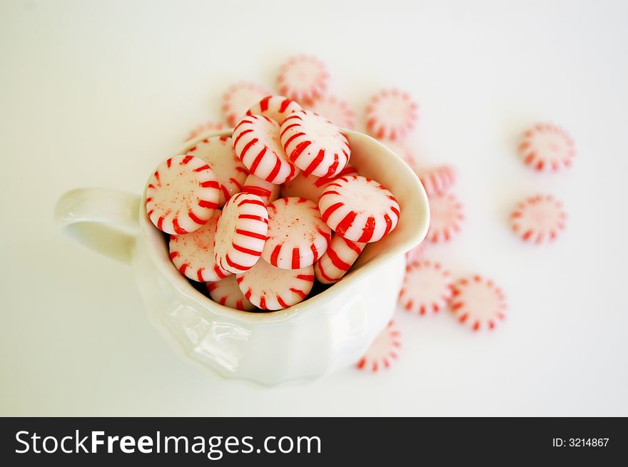 Red and white peppermint candy in  ceramic pitcher, scattered candies in background. Red and white peppermint candy in  ceramic pitcher, scattered candies in background
