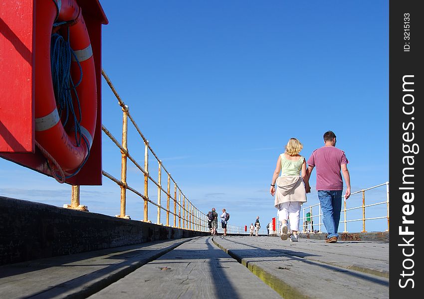 Young couple enjoy strolling on Whitby pier on sunny day. Whitby, North Yorkshire, UK.