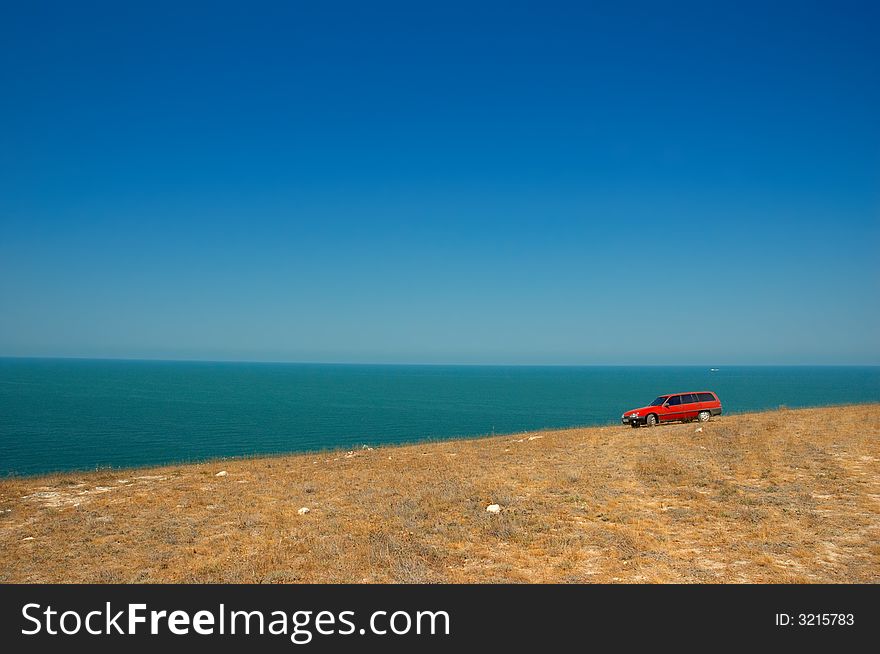 Red car on the slope on the sky and sea background