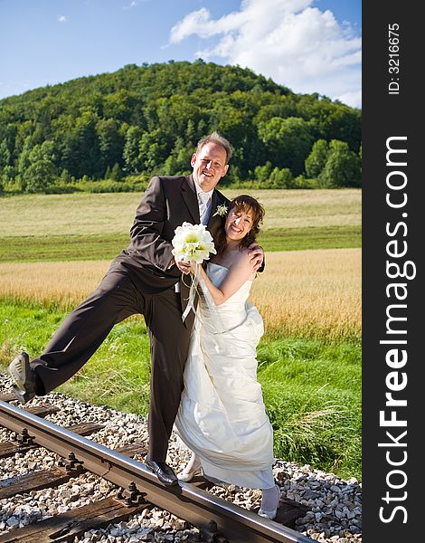 Bridal couple on rails, being in the nature. Great azure sky. Great summer! He balances on one foot on the rail. Bridal couple on rails, being in the nature. Great azure sky. Great summer! He balances on one foot on the rail.