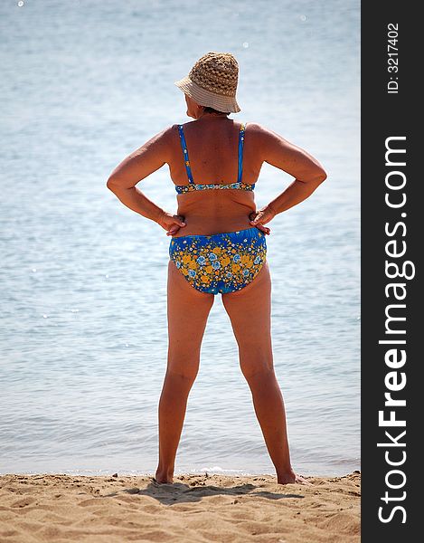 A woman with bikini and hat standing at the beach in a sunny day. A woman with bikini and hat standing at the beach in a sunny day.