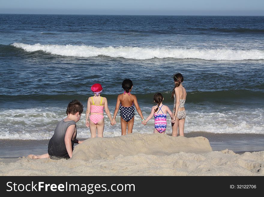 Little girls holding hands going into the ocean at a beach. while boy plays in sand. Little girls holding hands going into the ocean at a beach. while boy plays in sand