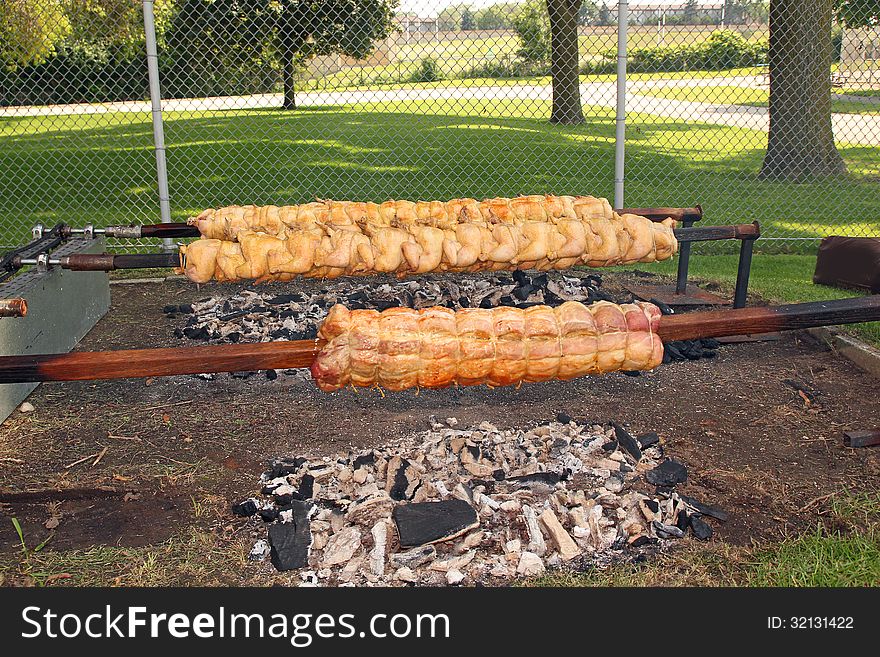 Fresh chicken and pork loin being roasted to a golden brown on a spit, over hot charcoal. Photo taken July 4, 2013. Fresh chicken and pork loin being roasted to a golden brown on a spit, over hot charcoal. Photo taken July 4, 2013.