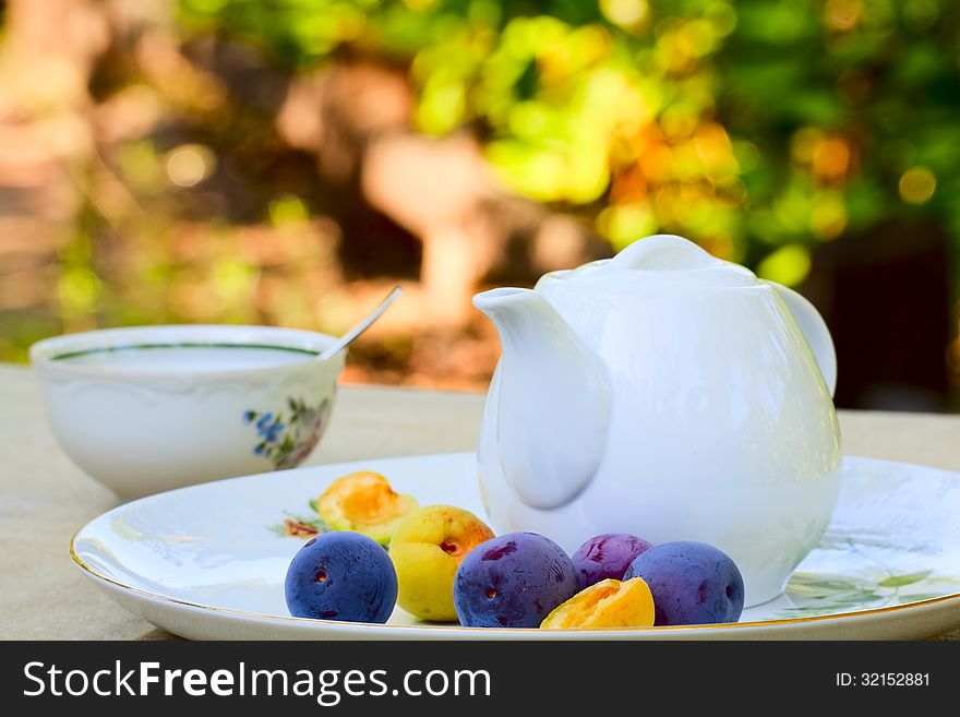 Summer morning tea - tea cup, teapot, plums and apricots on a platter